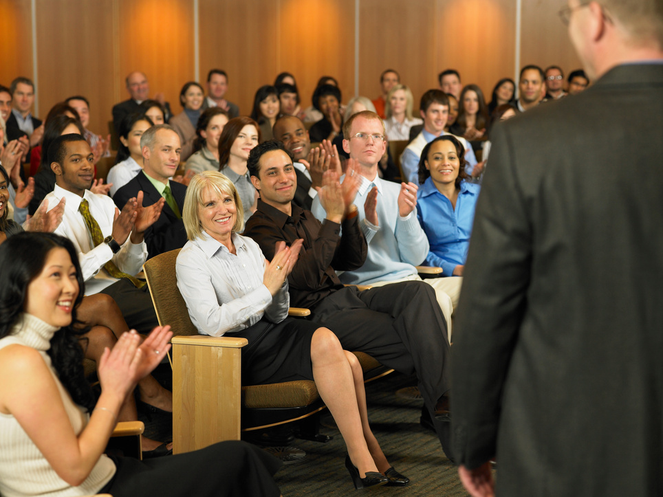 Group of executives applauding for man leading seminar in auditorium